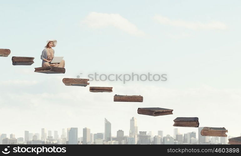 Romantic woman using laptop. Woman in dress and hat sitting on books and working on laptop