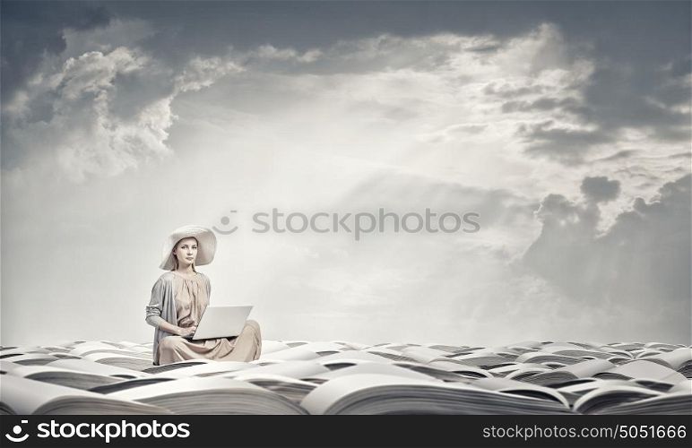Romantic woman using laptop. Woman in dress and hat sitting on books and working on laptop