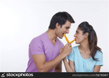 Romantic young couple feeding each other ice lollies over white background