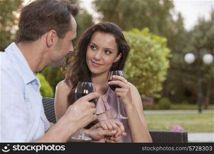 Romantic young couple holding hands while having red wine in park