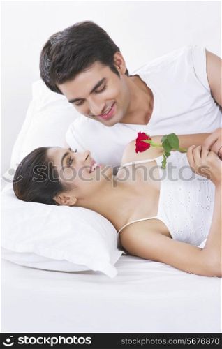 Romantic young couple holding rose in bed