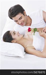 Romantic young couple holding rose in bed