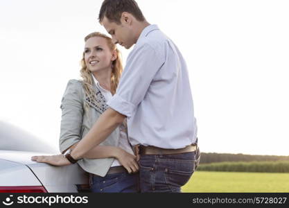 Romantic young couple leaning on back of car at countryside