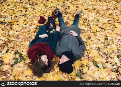 Romantic young couple lie on yellow leaves in park, hold hands together, look at each other with great love, enjoy autumn sunny day. People, relationships, togetherness and romance concept