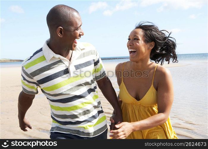 Romantic Young Couple Running Along Shoreline Of Beach Holding Hands