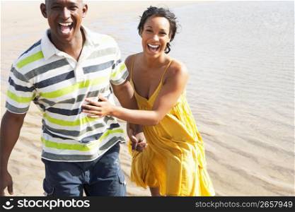 Romantic Young Couple Running Along Shoreline Of Beach Holding Hands