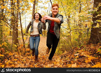 Romantic young couple running through autumn forest