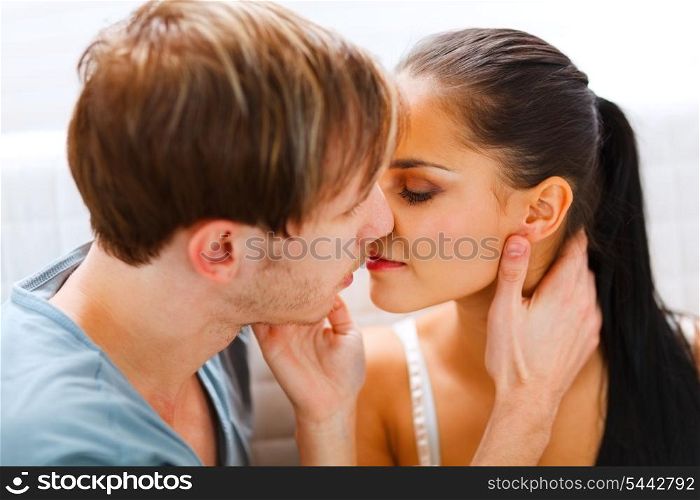 Romantic young couple sitting on divan and kissing&#xA;