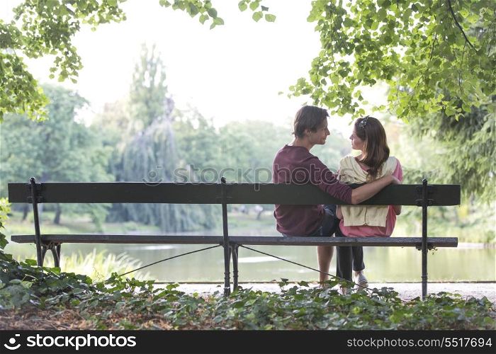 Romantic young couple sitting on park bench by lake