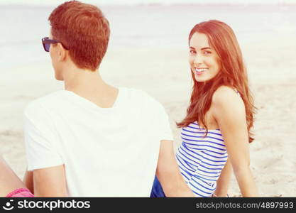 Romantic young couple sitting on the beach. Romantic young couple sitting on the beach looking at each other