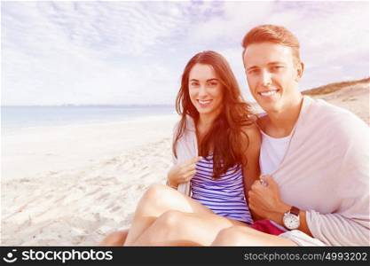 Romantic young couple sitting on the beach. Romantic young couple sitting on the beach looking at the camera