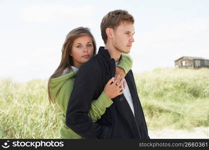 Romantic Young Couple Standing By Dunes With Beach Hut In Distance