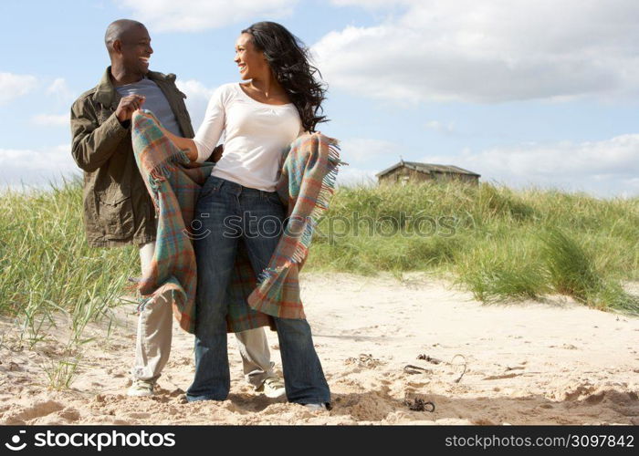 Romantic Young Couple Standing By Dunes With Beach Hut In Distance