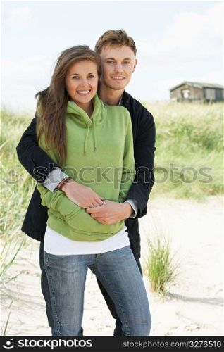 Romantic Young Couple Standing By Dunes With Beach Hut In Distance