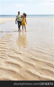 Romantic Young Couple Walking Along Shoreline Of Beach Holding Hands
