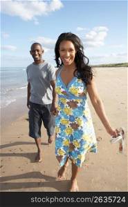 Romantic Young Couple Walking Along Shoreline Of Beach Holding Hands