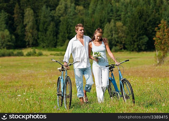 Romantic young couple walking with old bike in meadow on sunny day