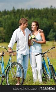 Romantic young couple walking with old bike in meadow on sunny day