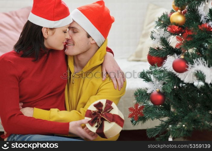 Romantic young couple with gift kissing near Christmas tree