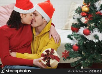 Romantic young couple with gift kissing near Christmas tree