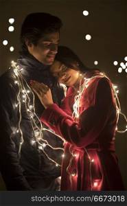 Romantic young couple wrapped in decorative lights
