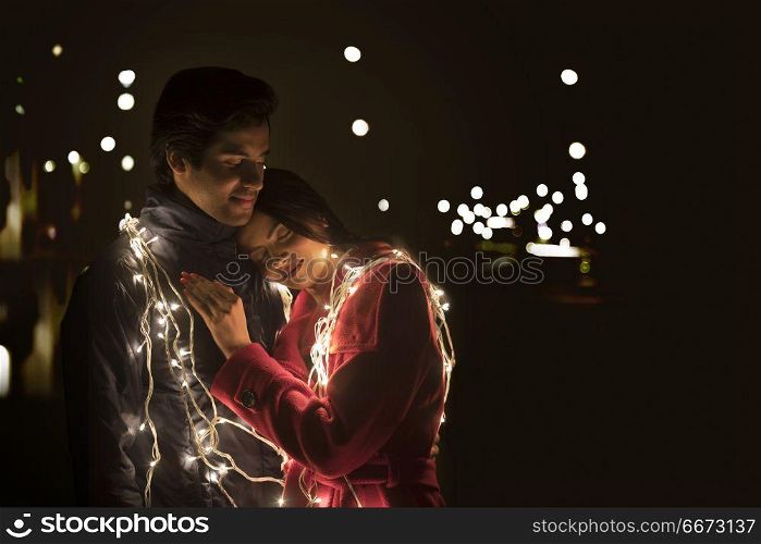 Romantic young couple wrapped in decorative lights