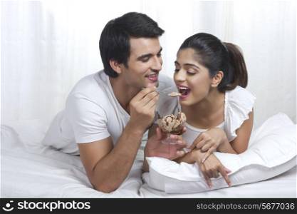 Romantic young man feeding woman chocolate ice cream in bed