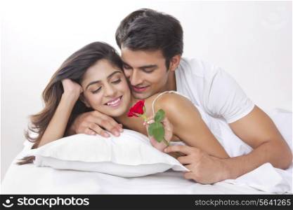 Romantic young man giving rose to woman in bed