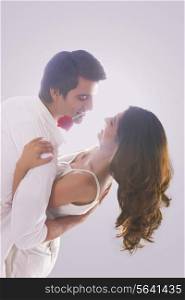 Romantic young man holding red rose in mouth while dancing with woman over white background