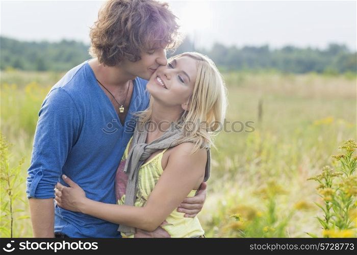Romantic young man kissing woman in field