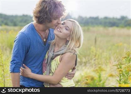 Romantic young man kissing woman in field