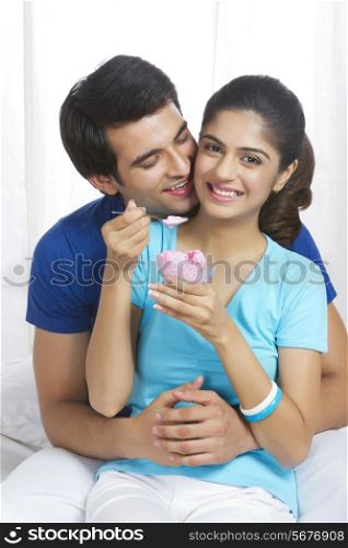 Romantic young man with woman eating ice-cream in bedroom