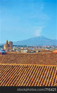Roofs of the old town of Catania and Mount Etna volcano with smoke, Sicily, Italy