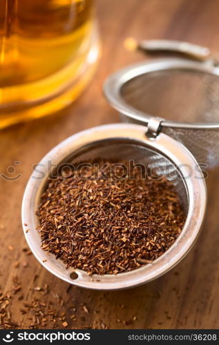 Rooibos herbal tea in strainer with freshly prepared tea in the back, photographed with natural light (Selective Focus, Focus one third into the leaves)