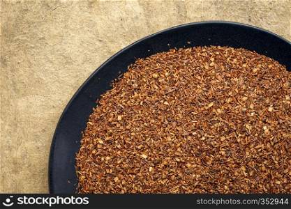 rooibos tea, made from the South African red bush, naturally caffeine free - overhead view of black plate against textured bark paper