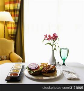 Room service cheeseburger meal with flowers and condiments.