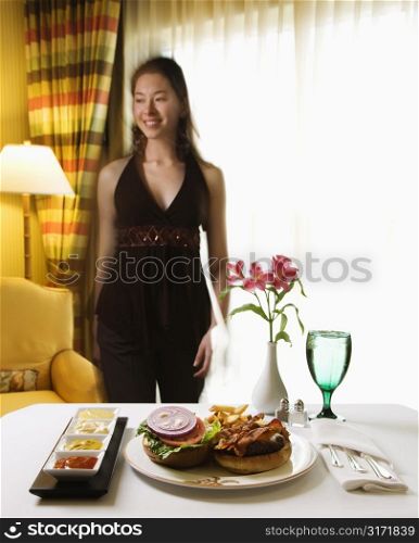 Room service cheeseburger meal with flowers and Taiwanese mid adult woman in background.