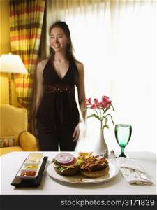Room service cheeseburger meal with flowers and Taiwanese mid adult woman in background.