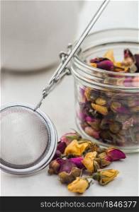 Rose buds mix tea in glass jar with vintage strainer infuser on white background.