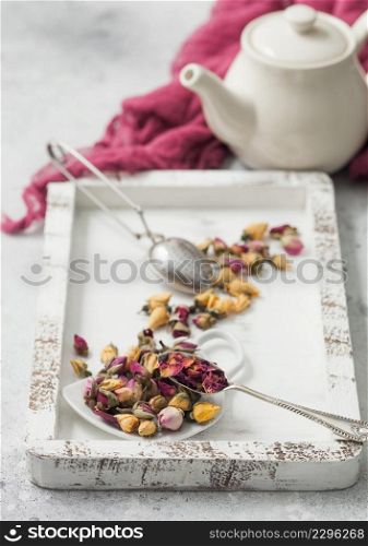 Rose buds mix tea in wooden box with tea vintage strainer infuser and teapot on white table background with red cloth.