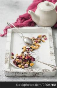 Rose buds mix tea in wooden box with tea vintage strainer infuser and teapot on white table background with red cloth.