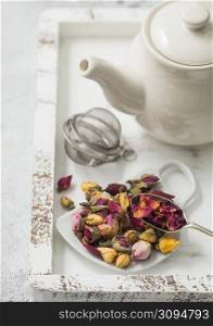 Rose buds mix tea on cup shape ceramic plate and tea ball strainer infuser and ceramic teapot in white wooden box. Macro