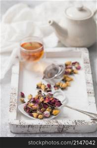 Rose buds mix tea with tea ball strainer infuser and teapot on white background with linen cloth and glass cup. Macro