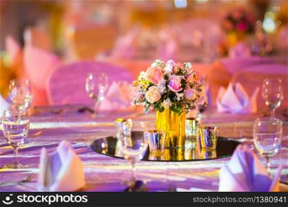 rose florist in glass vase decoration on dinner table with silverware and candle Indian wedding setup indoor with decorative lights and beautiful bokeh.
