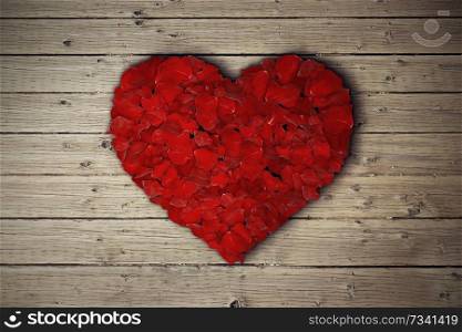 Rose petals arranged in shape of heart on wooden table. 