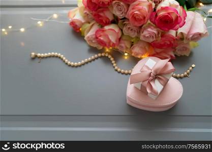 Rose pink flowers bouquet with jewellery on gray table with gift box from above, flat lay scene. fresh rose flowers on gray