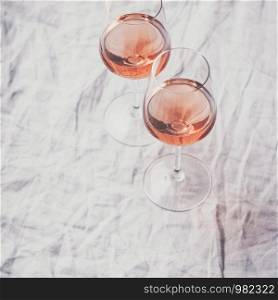 Rose wine in glasses on white linen cloth, flat lay