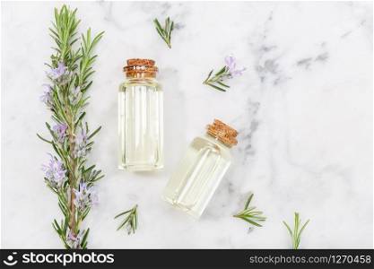 Rosemary essential oil in glass bottle and twigs on marble table. Salvia Rosmarinus oil. Top view