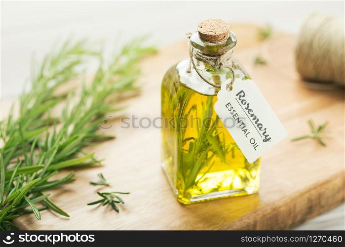Rosemary essential oil with tag, fresh twig on wooden background