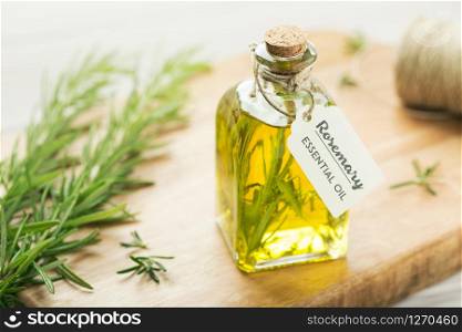 Rosemary essential oil with tag, fresh twig on wooden background